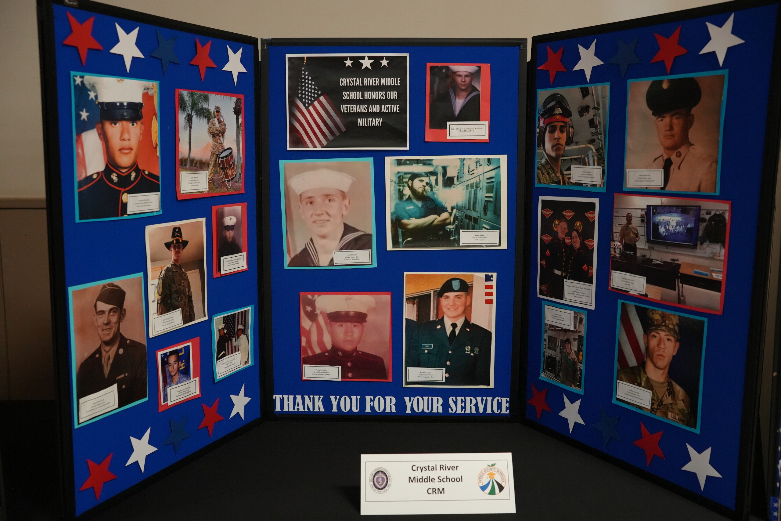 A trifold blue display board honors veterans and active military personnel with photos and stars.